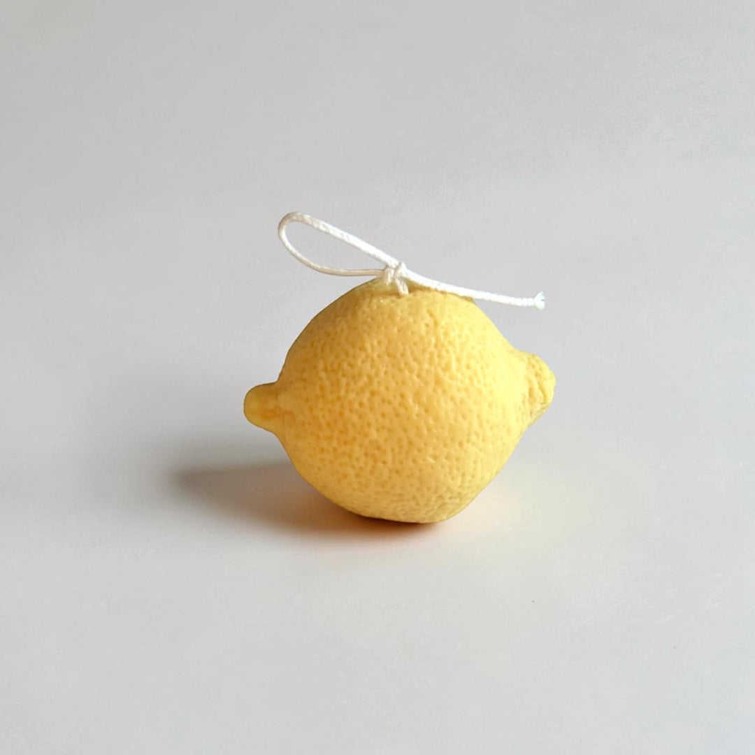 A small yellow lemon-shaped candle photographed on a plain light gray background.